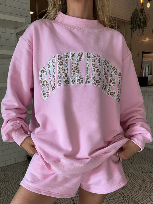 Person wearing a pink sweatshirt and shorts set with leopard print text, standing on a tiled floor.