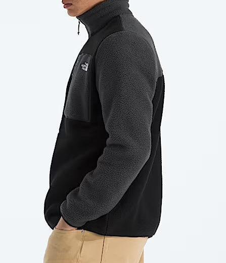 Person wearing a black fleece jacket with a logo on a white background