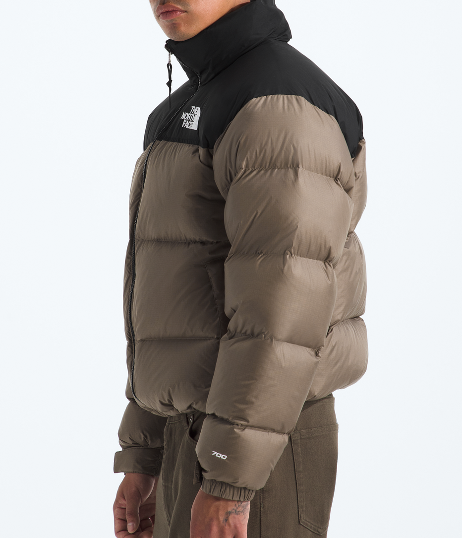 Person wearing a brown puffer jacket and black cap on a white background