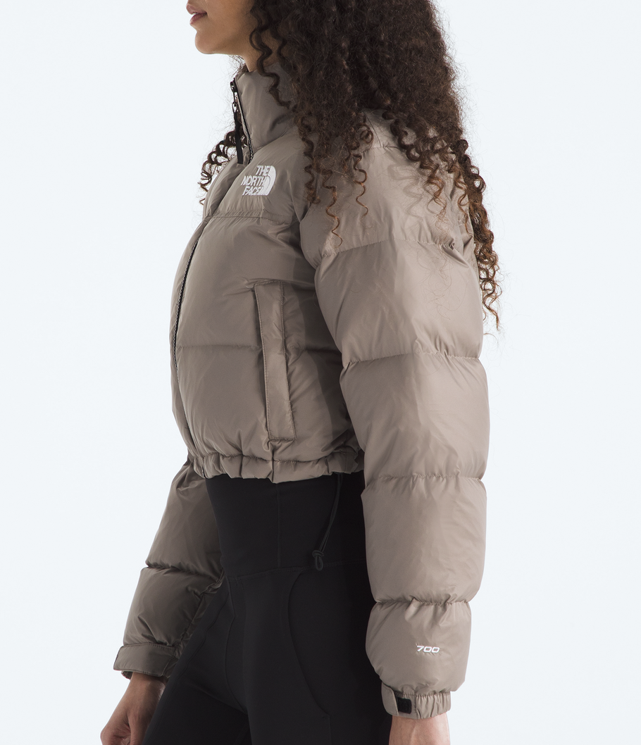 Woman wearing a beige puffer jacket with The North Face logo on a white background 