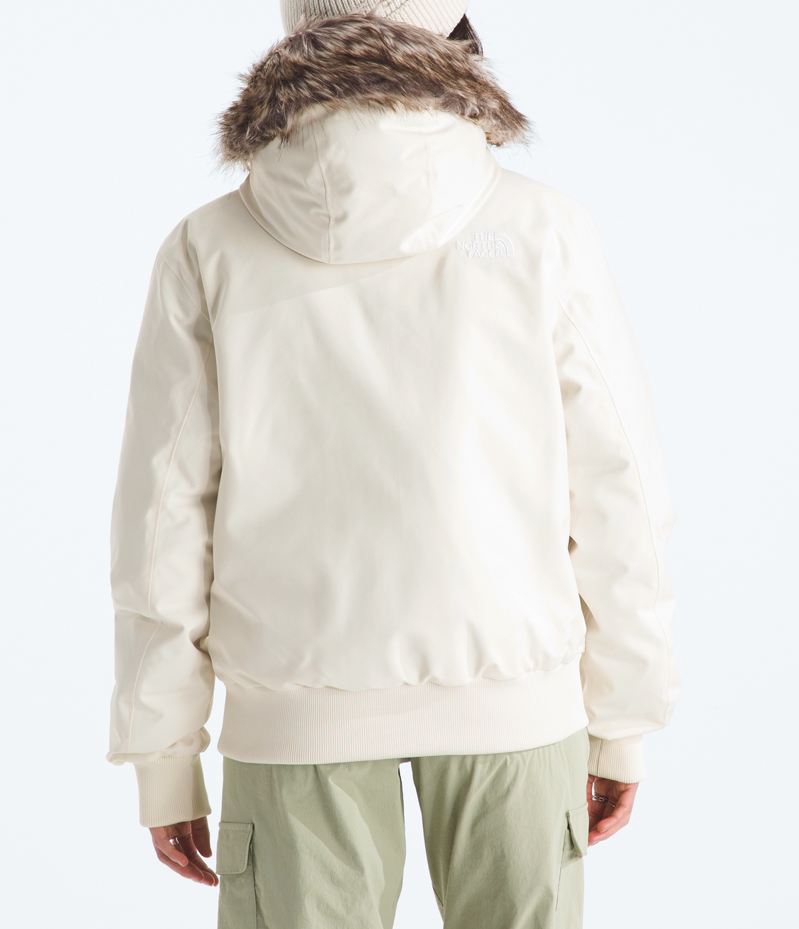 Person wearing a cream-colored jacket with fur hood and light green pants on a white background 