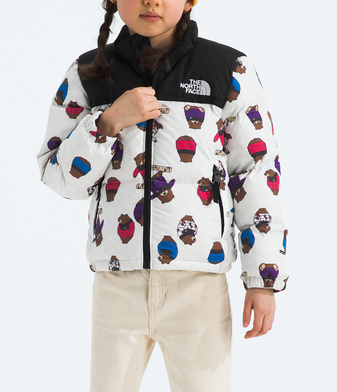 Child wearing a patterned jacket, beige pants, and a yellow beanie on a white background