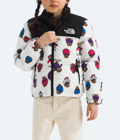 Child wearing a patterned jacket, beige pants, and a yellow beanie on a white background