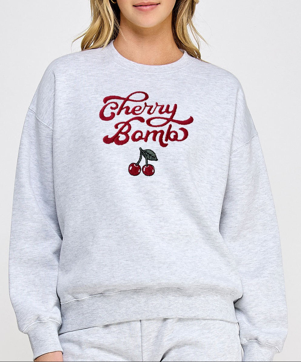 Person wearing a gray sweatshirt with 'Cherry Bomb' text and cherry graphics on a plain background