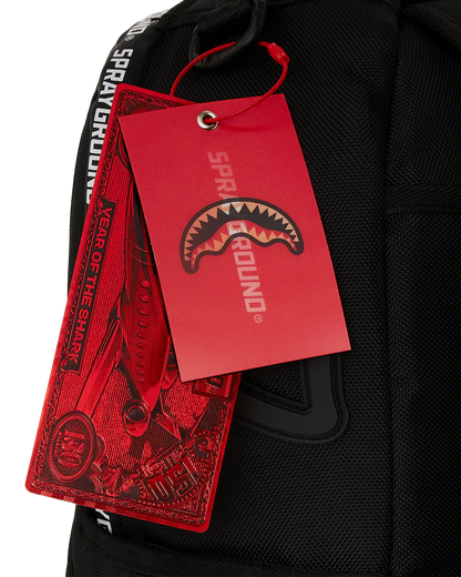 Black backpack with a red 'Sprayground' tag featuring a shark logo.
