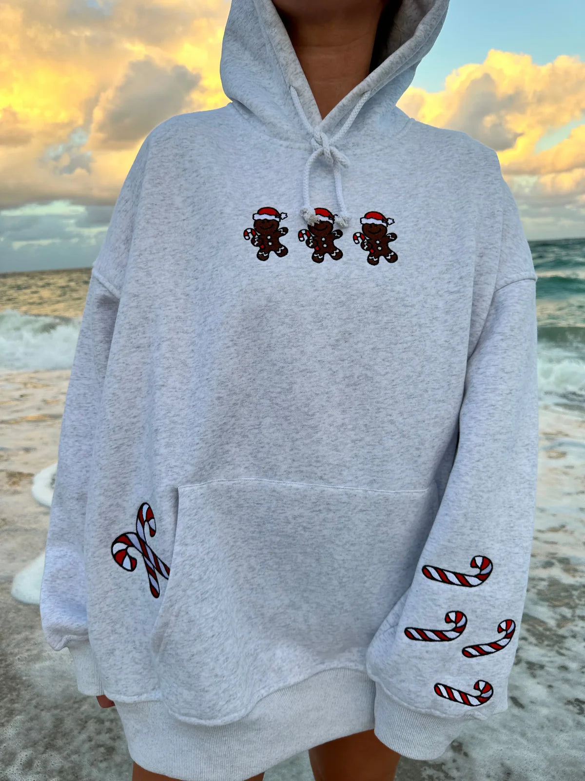 Gray hoodie with Christmas-themed designs on a beach at sunset