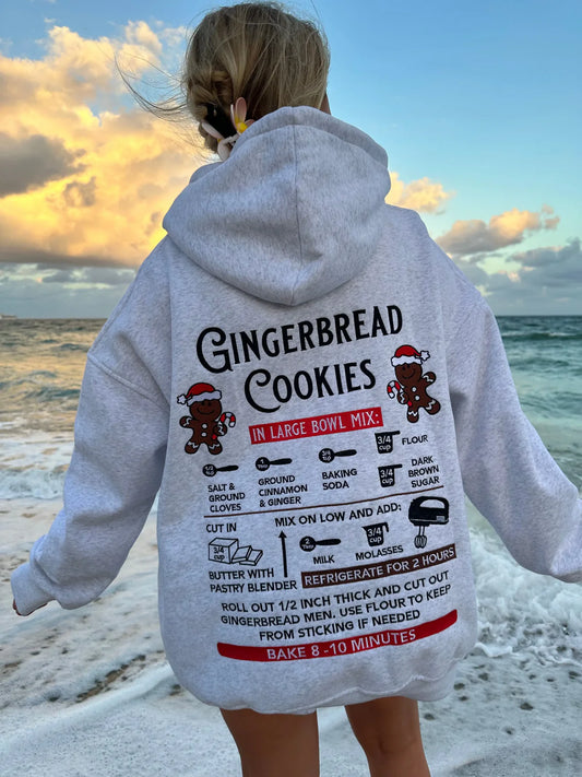 Person wearing a hoodie with a gingerbread cookies recipe design at the beach.