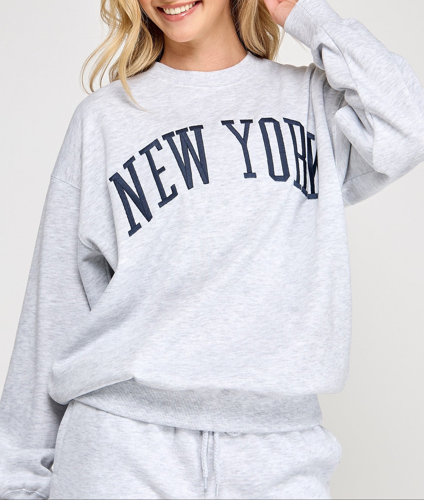 Woman wearing a gray 'New York' sweatshirt on a white background