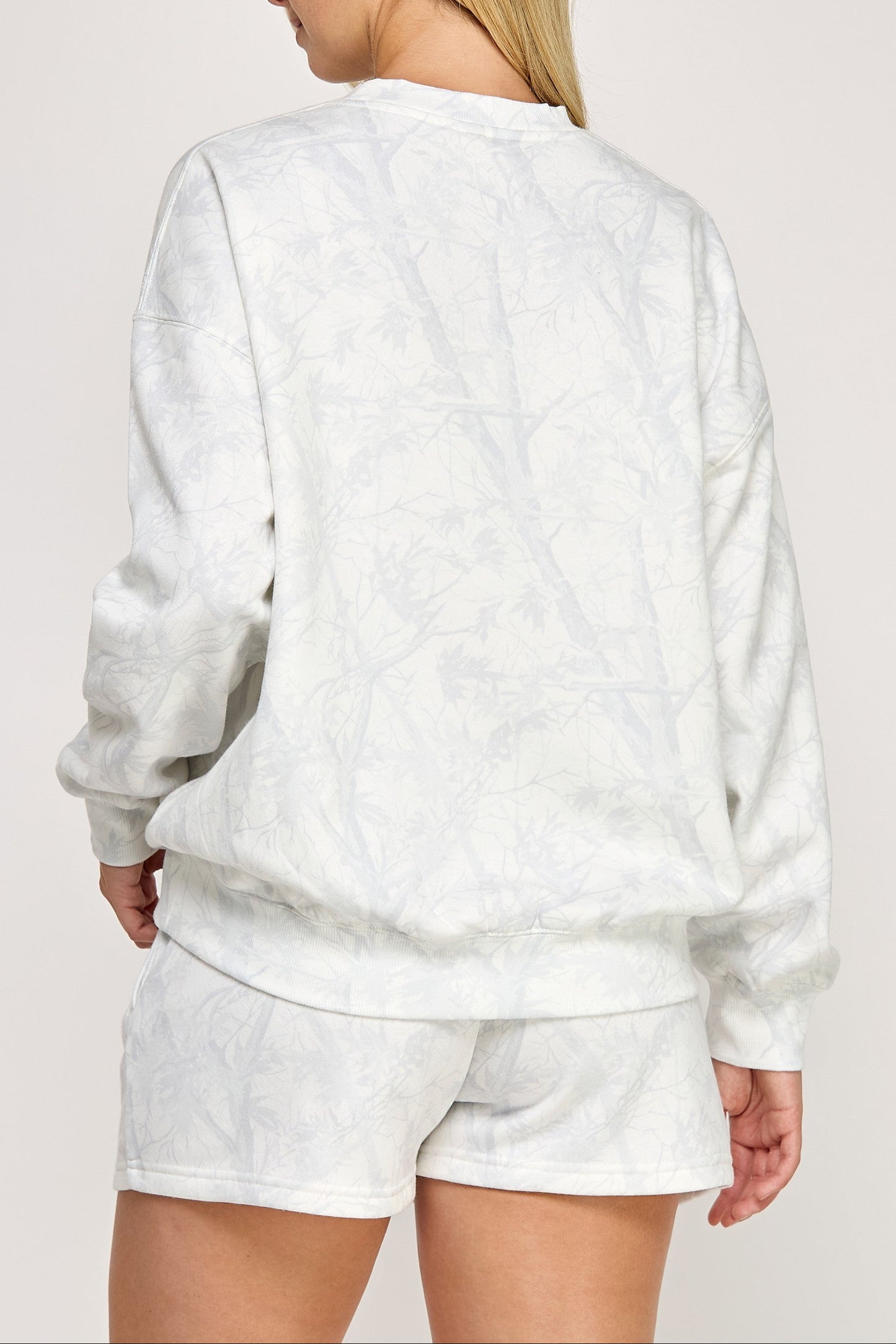 Person wearing a white sweatshirt and shorts set on a plain background