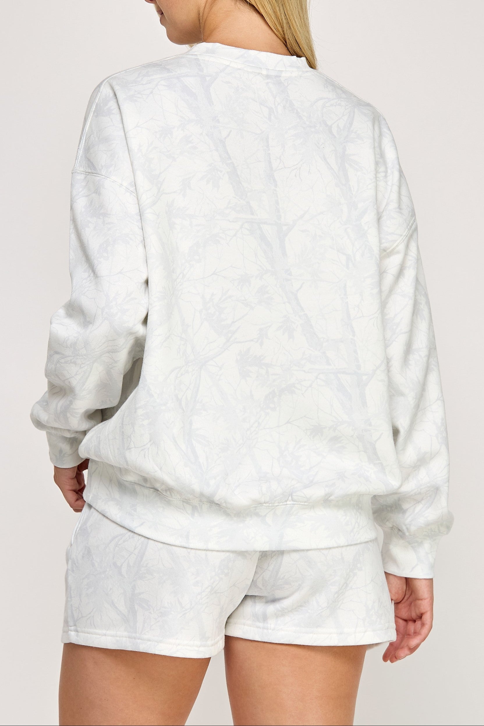 Person wearing a white sweatshirt and shorts set on a plain background